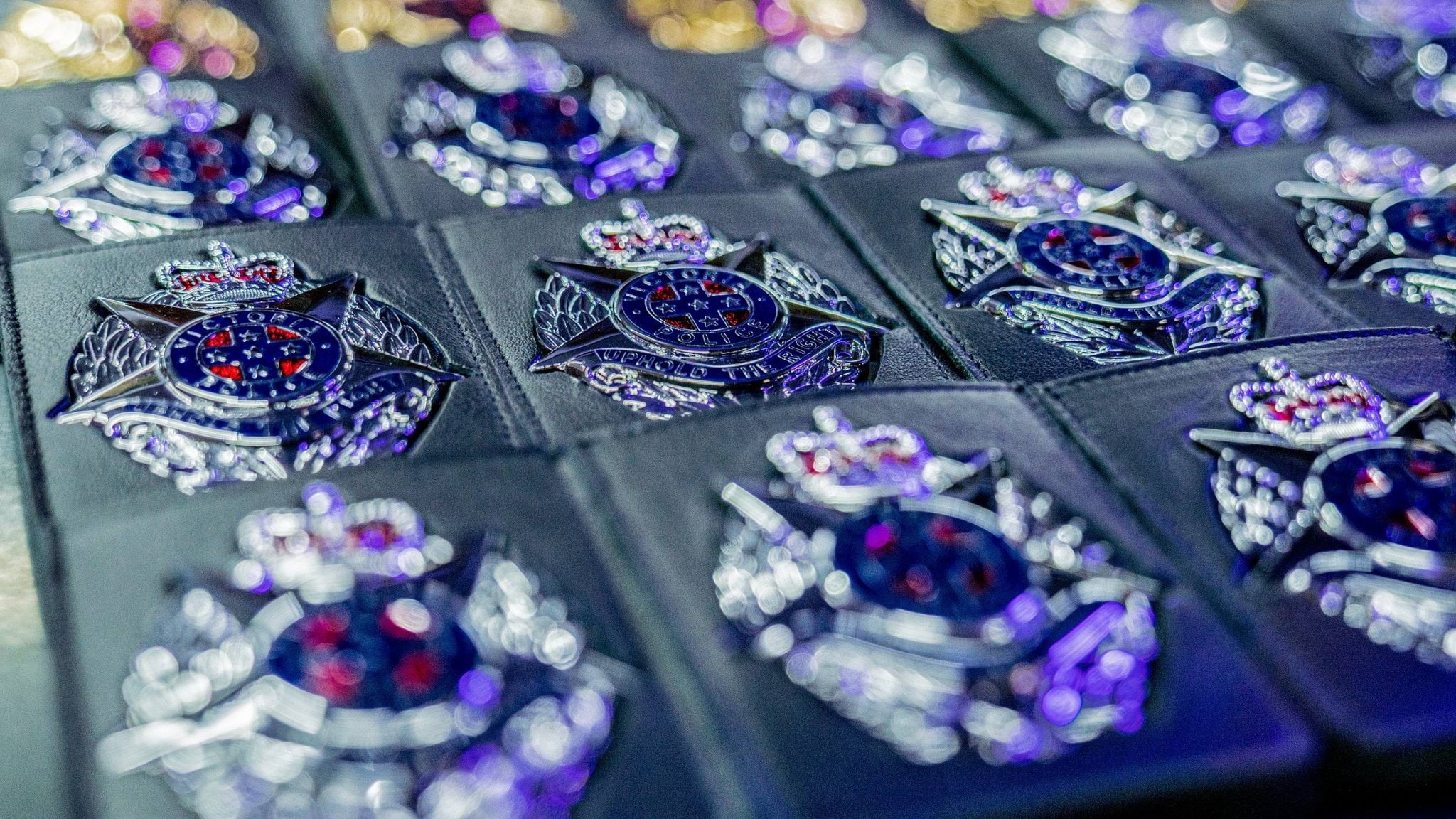 Mental health, resilience and wellbeing in the Police Display of silver police badges in their black, pocket-size holders lined up on display. Badge image is a silver star on an oval shaped background, with a crown resting on the top point of the star. Text on the badge reads Victoria Police, Uphold the Right.