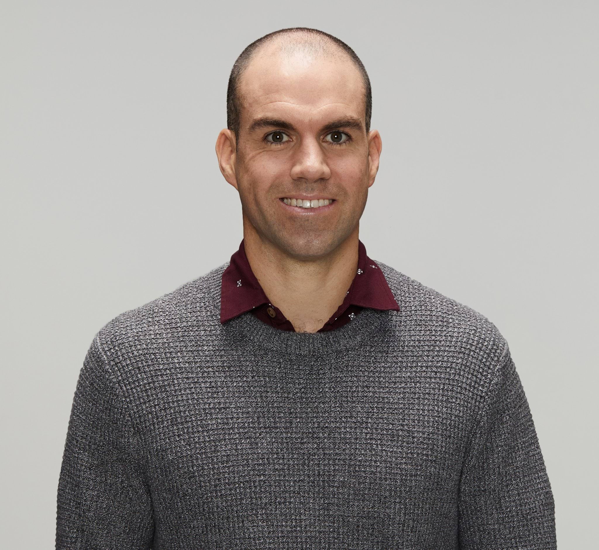 Mark's lived experience Police officer in civilian clothing smiling at the camera. White male, early forties with dark receding hair, wearing a maroon collared shirt with a smart casual metal grey jumper over the top.