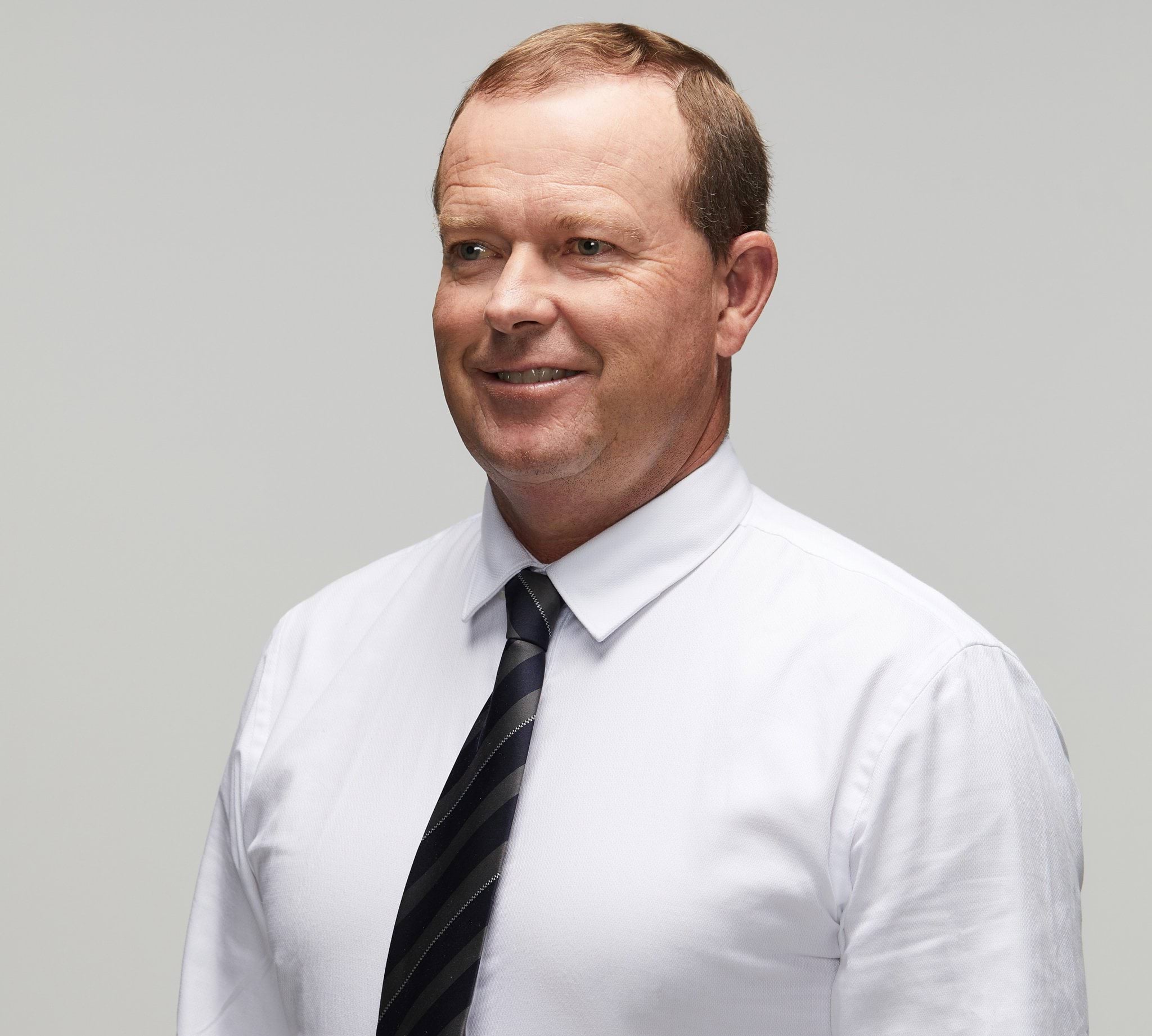 Peter B.s story Police officer in civilian clothing smiling to left of camera, wearing long-sleeved white shirt with black and silver stripped tie; white male, mid to late forties with thinning nutbrown, coloured hair