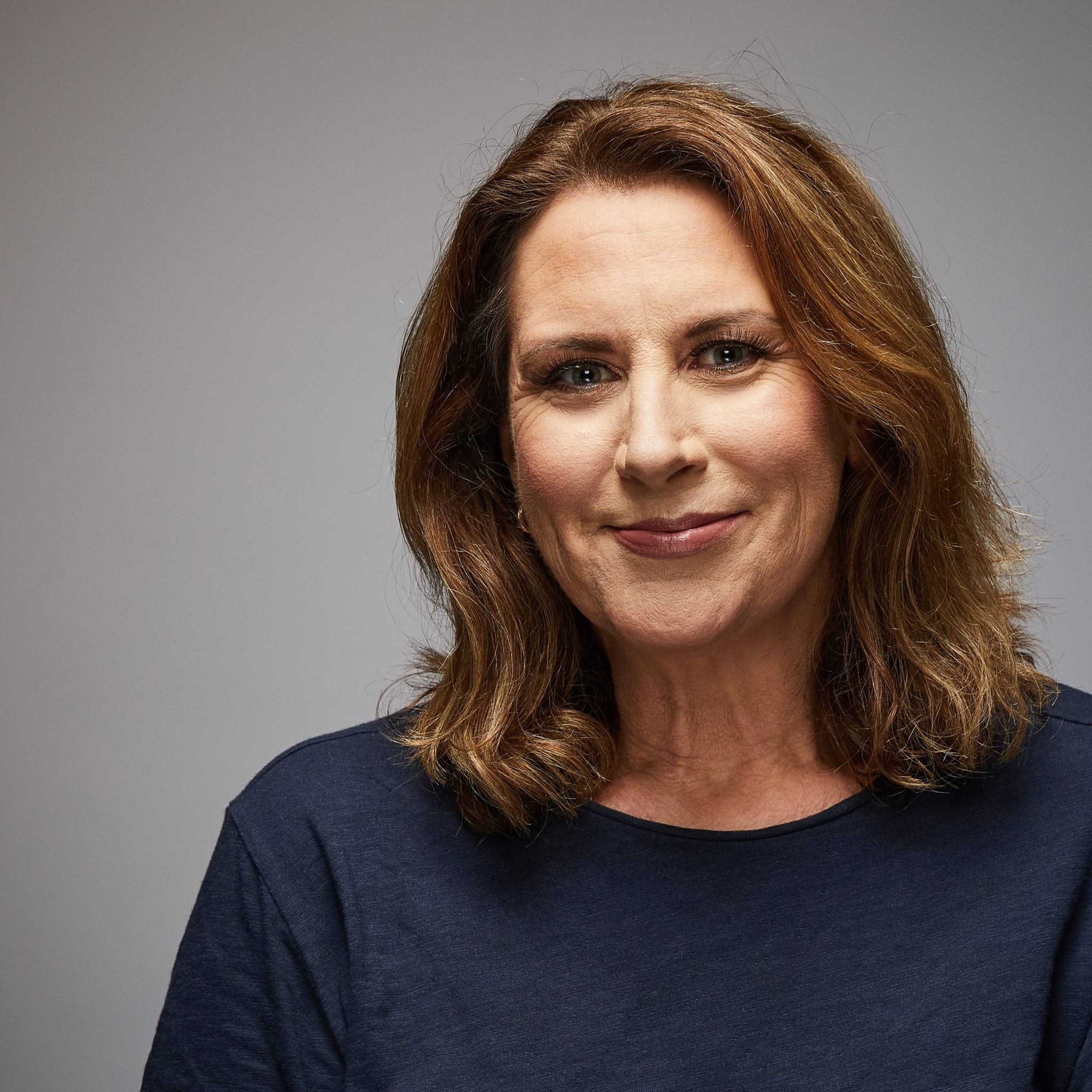 Rose's story Female police officer in civilian clothing smiling at camera, wearing long-sleeved smart casual navy blue top; Caucasian female, mid to late forties with shoulder-length honey brown, coloured hair
