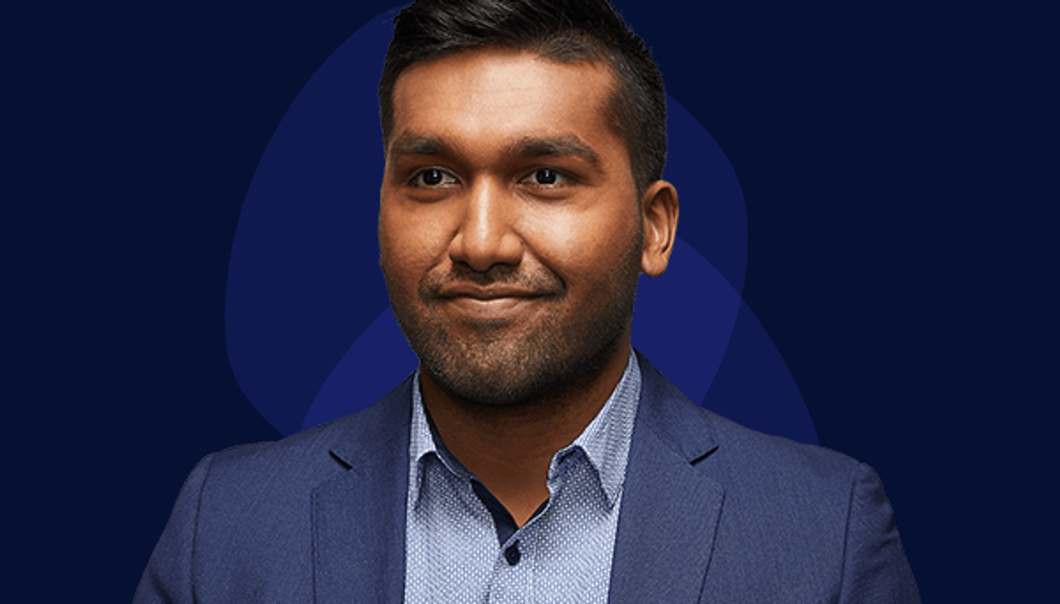 Image of current VPS employee looking slightly off camera to the left wearing a light blue shirt with a dark blue suit jacket. Male aged late twenties/early thirties with dark skin, slight beard stubble, and black hair